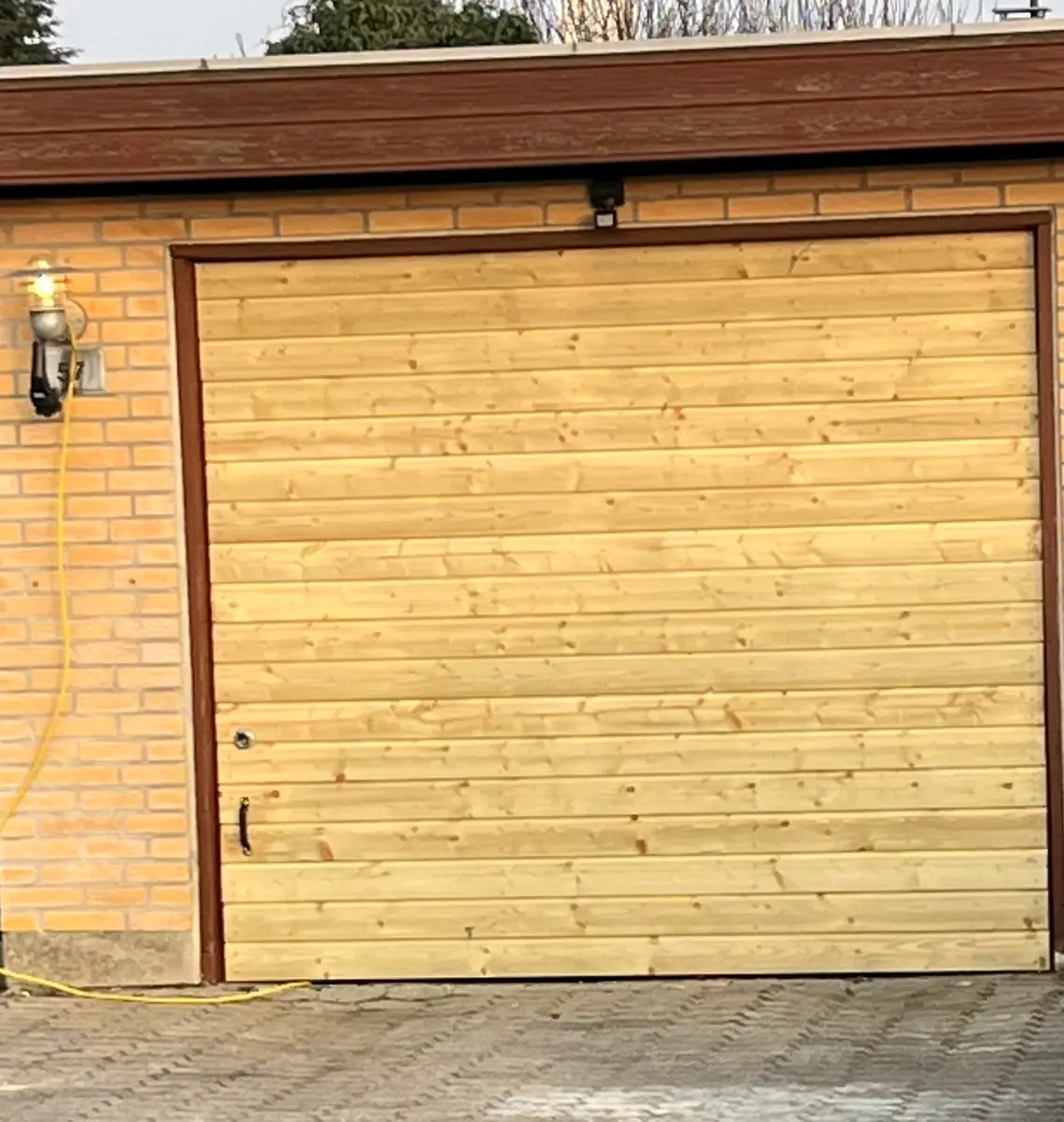 Garageport beklædt med nye vandrette brædder i lyst træ, gulstensvæg og brun trælistefacade omkring