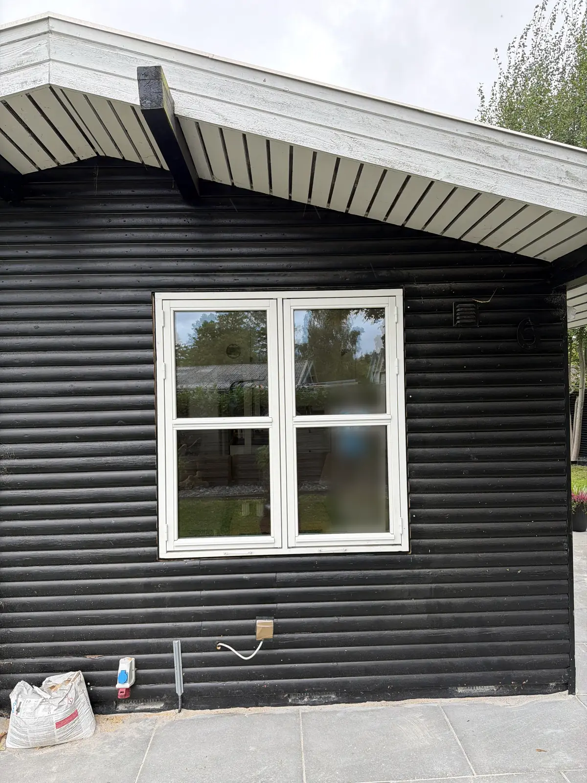 Nyt hvidt vindue med fire ruder i den sorte bjælkegavl under det hvide udhæng, med flisebelagt terrasse foran